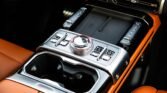 Center console of a luxury car with a large chrome rotary dial, metal buttons, and orange leather interior.