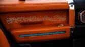 Orange leather car door panel with a dotted perforated pattern and a blue ambient light strip along the lower edge, in a luxury interior.