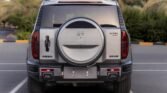 Rear view of a silver SUV with a mounted spare tire cover on the back, parked in an empty parking lot.