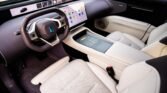 Luxurious car interior with white perforated seats, wide touchscreen dashboard, and a minimalist center console viewed from the driver’s seat.