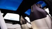 Luxurious car interior with cream leather seats and a large blue panoramic sunroof; front seats visible from the rear passenger area.