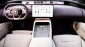 Interior of a modern car with a large tablet-style infotainment screen, tan steering wheel, and light beige seats.