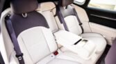 Back seat of a luxury car with light beige leather, three seat belts, and a fold-down center armrest.