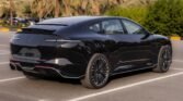 Black luxury sedan parked in a sunny parking lot, glossy finish and multi-spoke wheels visible with palm trees in the background