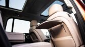 Interior of a luxury car with beige leather seats, a fold-out tray on the back of the front seat, and a panoramic sunroof.