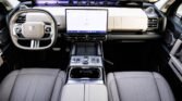 Luxurious car interior with a large central touchscreen, digital gauges, and beige leather seats.