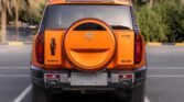 Orange SUV parked in a lot, rear view showing a circular spare-tire cover and taillights on each side.