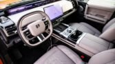 Luxury car interior with a light gray leather steering wheel and center console, large touchscreen dashboard, and cupholders in the center