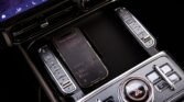 Center console of a luxury car with a smartphone resting on a wireless charging pad amid chrome controls and ambient lighting, viewed from above.