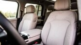 Interior of a luxury car with light gray perforated leather seats, front row, and a beige headrest visible through the sunroof window