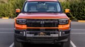 Front view of a bright orange off-road pickup truck parked in a lot, black grille and large tires visible.