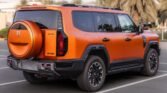 Orange GMC Hummer EV SUV parked in a lot, rear view showing the spare tire cover and rugged design.