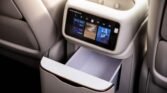 In-flight entertainment touchscreen on the back of a-seat console with a lowered tray/table and surrounding beige cushions.