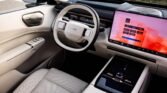 Luxurious car interior with light-colored seats, a circular steering wheel, and a large dashboard touchscreen displaying a pink interface.