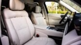Luxury car interior with light beige leather seats and a central console area that includes controls, seen from the front passenger seat.