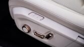 Close-up of a car seat's power-adjustment panel on light leather, showing memory buttons (1, 2, M) and chrome controls