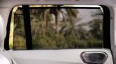 Mesh sunshade across a car's rear side window, obscuring a blurred green landscape outside (luxury SUV interior).