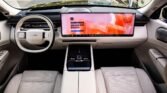 Modern car interior with a large horizontal touchscreen display across the dashboard and light perforated seats.