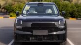 Front view of a shiny black SUV parked in a marked parking space, showing vertical LED headlights and a wide grille.