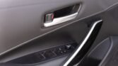 Car interior door panel with a chrome door handle and window/lock controls along a stitched black armrest panel.