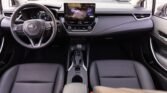 Front interior of a modern car showing a steering wheel, large central touchscreen, and black leather seats.