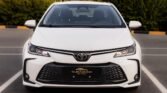 Front view of a white Toyota sedan in a parking lot, showing the grille and emblem.