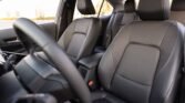 Front interior of a car with black leather seats, steering wheel in the foreground, and a center console between the seats.