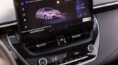 Infotainment screen in a car showing a white car graphic and navigation options, with hazard button and climate controls below.