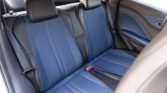 Rear car seat with blue and black leather upholstery, headrests, and a red seatbelt buckle visible between seats in a passenger vehicle.