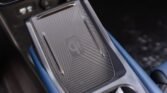 Car center console with a wireless charging pad marked by the Qi logo and diagonal stripes.