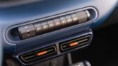 Close-up of a car's central control panel with a row of function buttons above a blue dashboard and orange-accented vents.