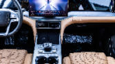 Luxurious car interior with a dual touchscreen dashboard, wood trim, and tan quilted seats in the front cabin